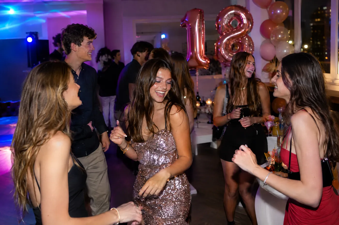 18th birthday in a flat: gold 1 and 8 balloons, friends dancing under coloured lights