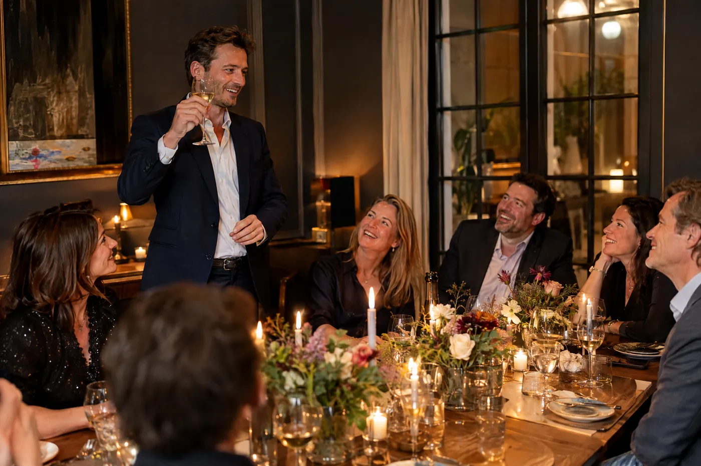 40th birthday dinner: a friend stands up to give a toast, the candlelit table laughing around him